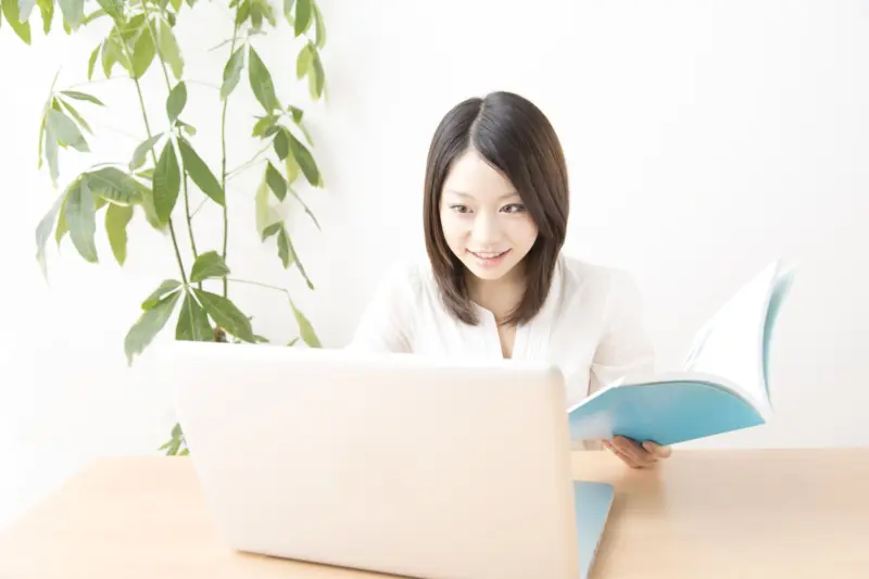 本を開きながらパソコンを見る女性